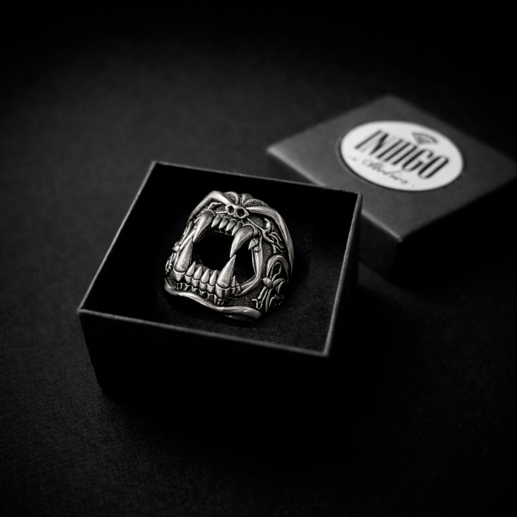 A close-up black and white image of a silver ring with a fierce, open-mouthed design, placed inside a black box.
