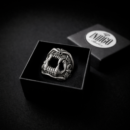 A close-up black and white image of a silver ring with a fierce, open-mouthed design, placed inside a black box.