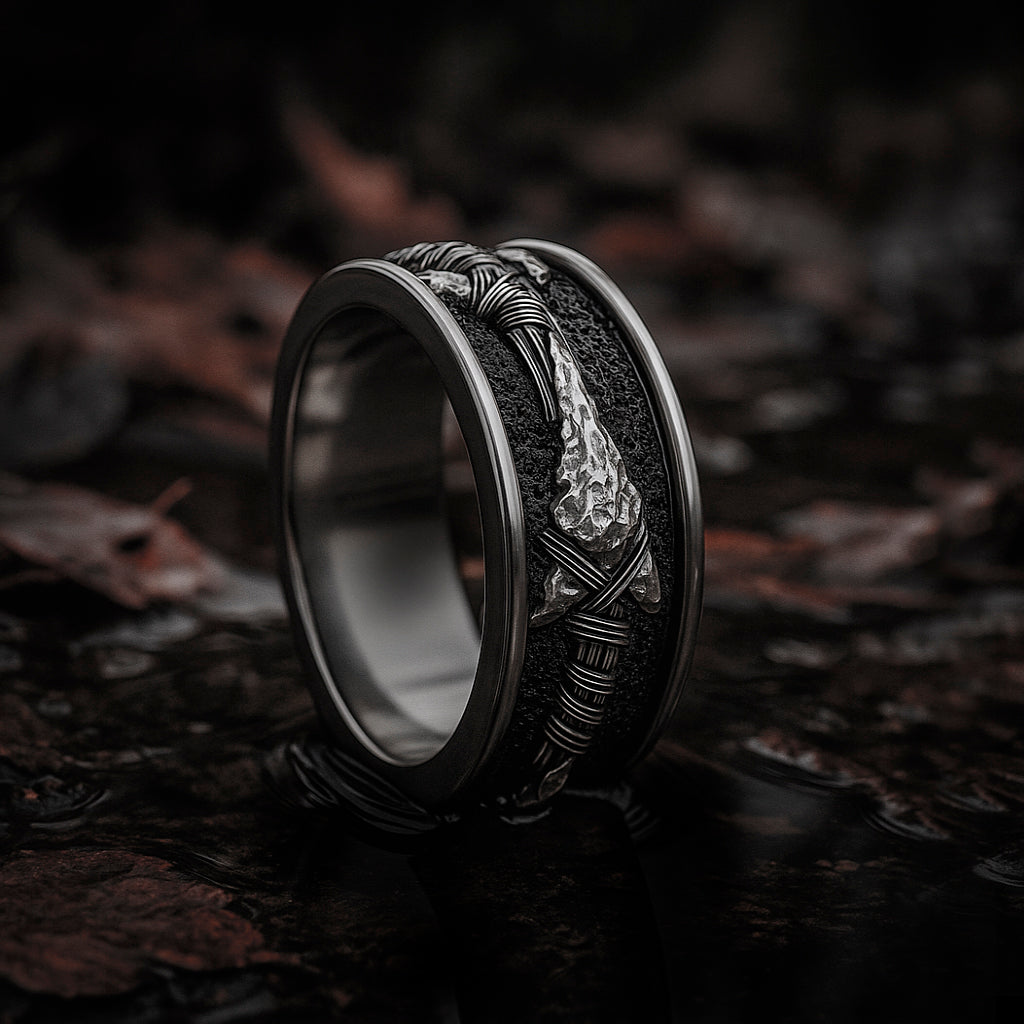 A silver ring with a unique design, featuring a metallic band and a decorative element, is displayed on a dark surface.
