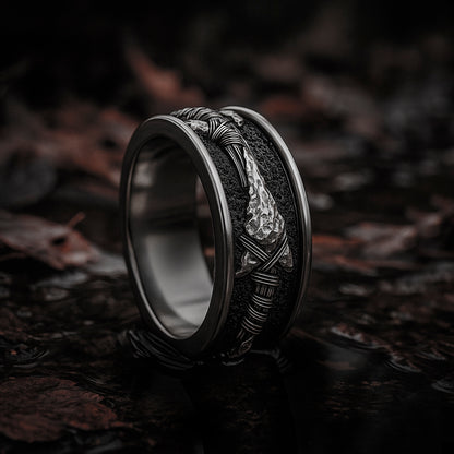 A silver ring with a unique design, featuring a metallic band and a decorative element, is displayed on a dark surface.