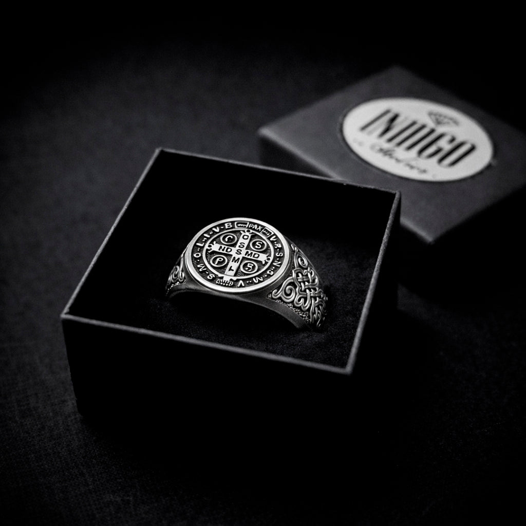 A silver ring with a circular design is displayed in a black box, with the ring box visible in the background.