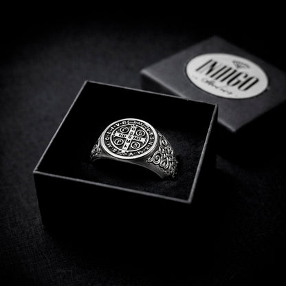 A silver ring with a circular design is displayed in a black box, with the ring box visible in the background.
