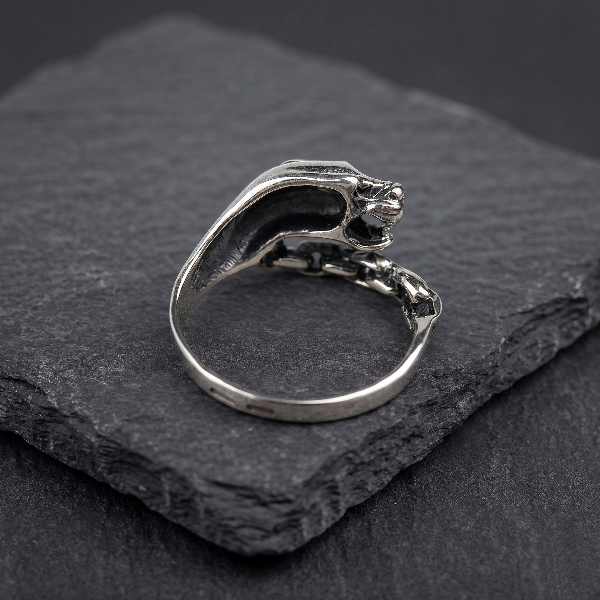 A silver ring with a silver Panthera head design and a chain-link chain attached to it. Green zircon in the eye. Indigo Jewelry. Backside.