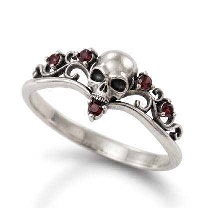 Dainty gothic engagement ring made of blackened 925 sterling silver, featuring a detailed skull design with red cubic zirconia gemstones. Elegant womens silver goth ring in a skull ring style, isolated on a clean white catalog background with a soft gradient shadow.