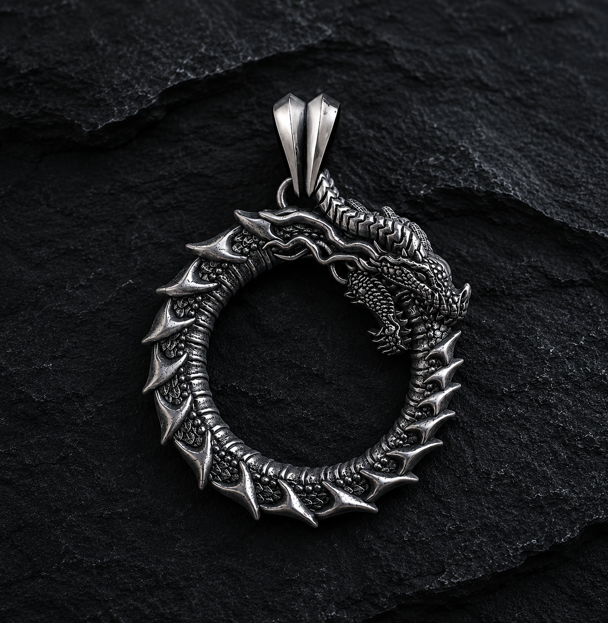 Ouroboros dragon pendant in oxidized sterling silver 925 by INDIGO Jewelry on a dark textured background. Handcrafted symbolic dragon necklace inspired by mythology, featuring detailed scales and an ancient eternity symbol.