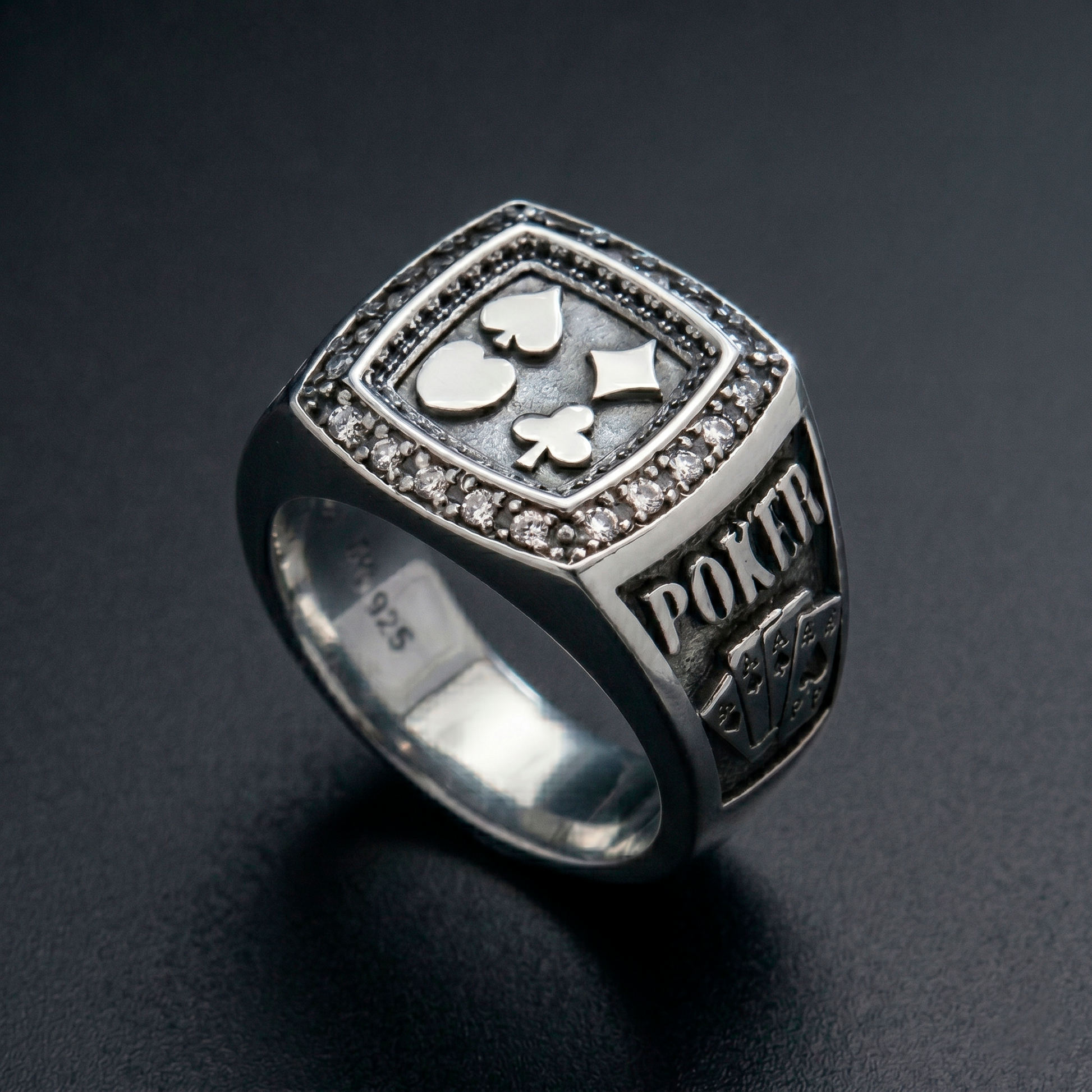 Men's sterling silver poker signet ring showcasing four card suits and embedded stones on a premium black background by Indigo Jewelry.